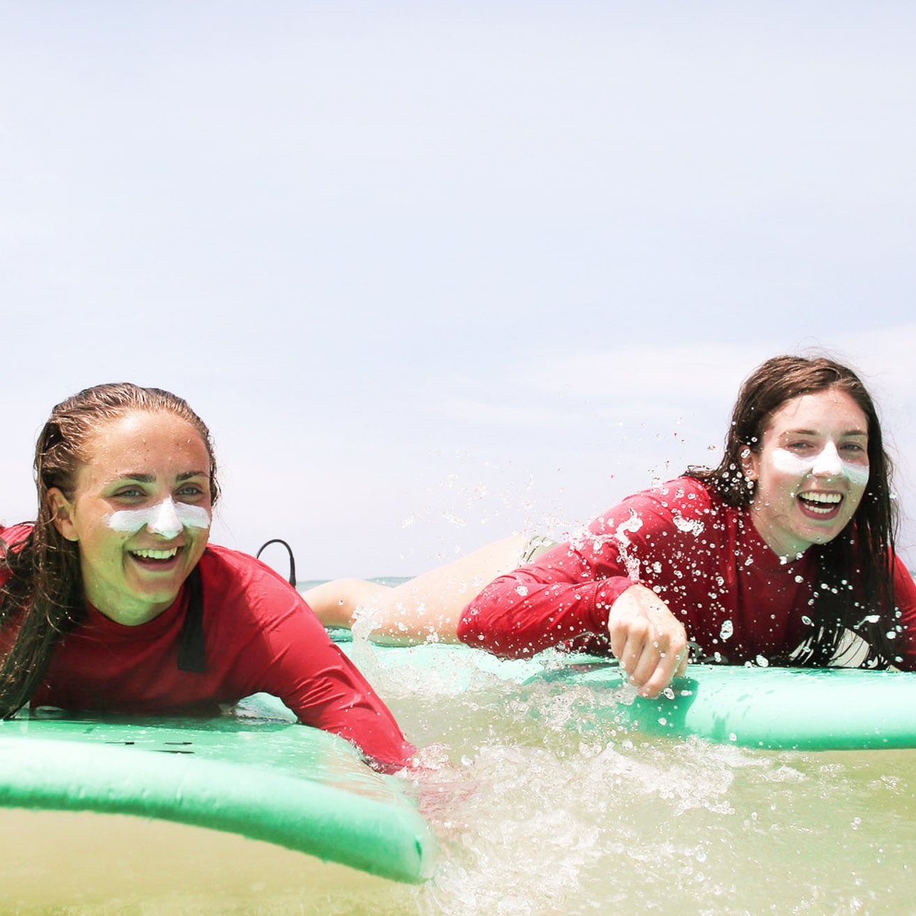 Two women surfing while using Suntribe natural zinc sunscreen.