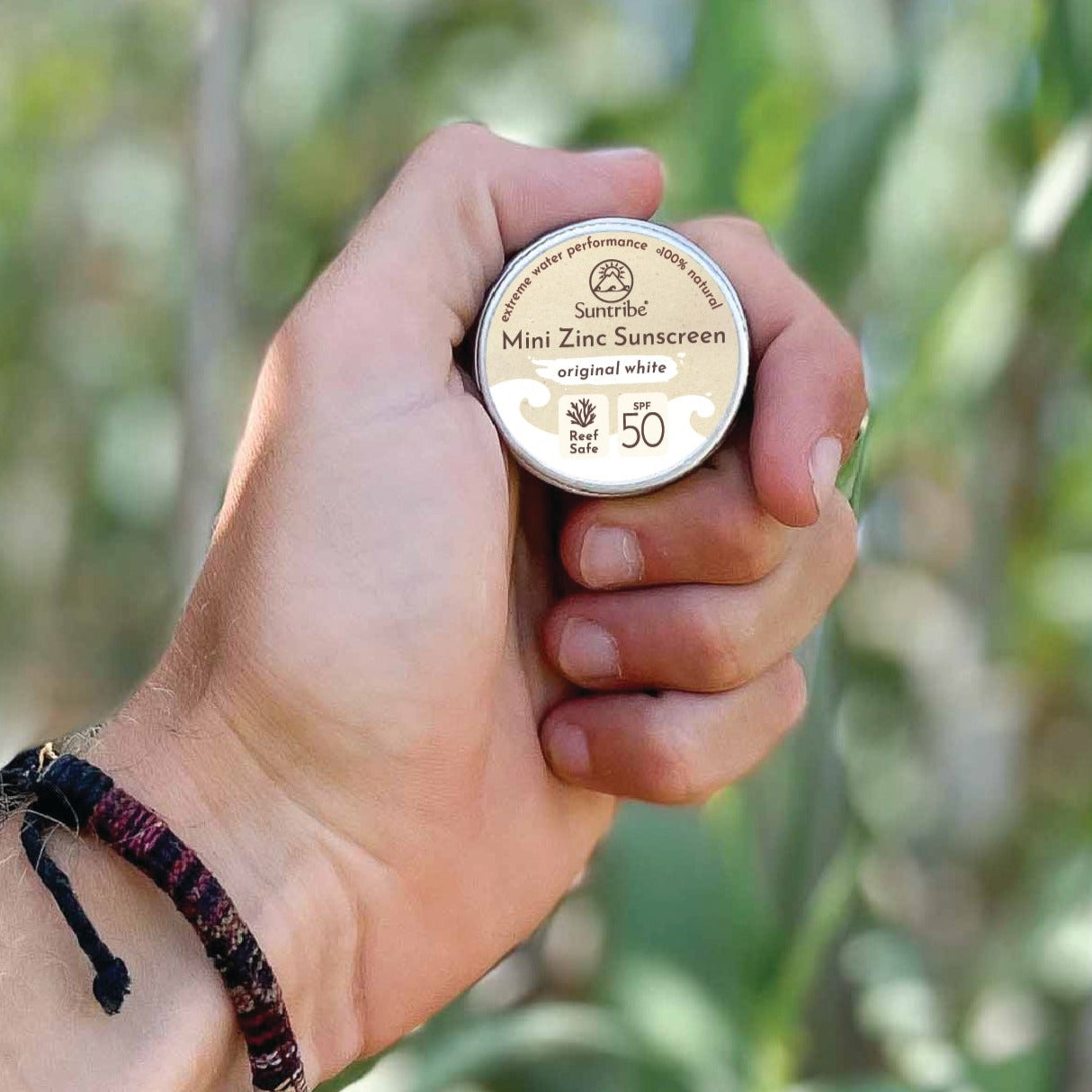 Closeup shot of a hand holding a tin of Suntribe natural zinc sunscreen.