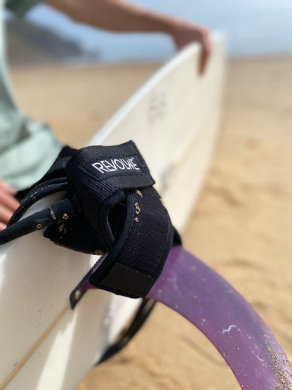 a Black REVOLWE surf leash wound around the back of a surfboard.