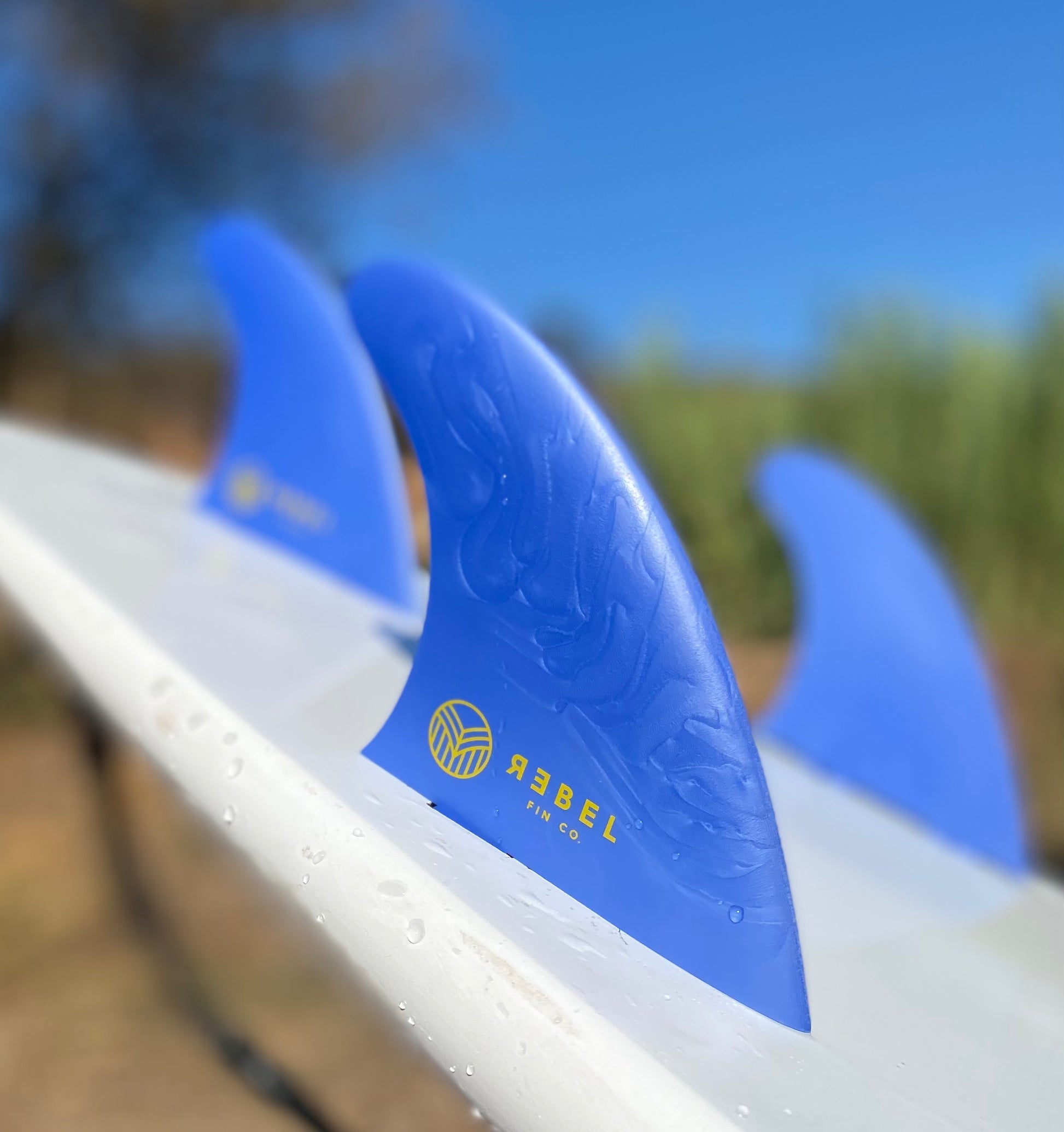 Blue thruster surfboard fins made by Rebel Fin Co. The surf fins are shown attached to the surfboard